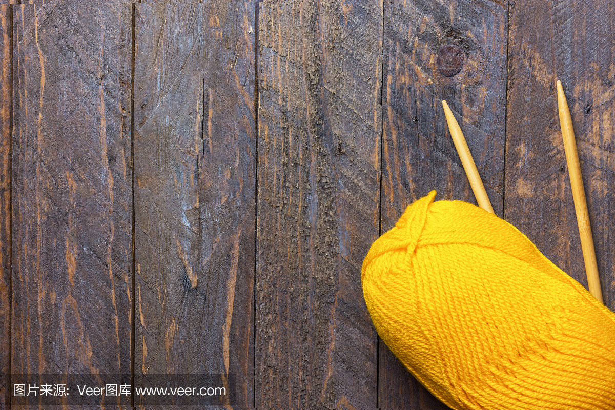黄色毛线针织针的线索在老化的木板木材背景。手工艺爱好服装制作时尚概念。温暖的颜色。极简主义的平面躺在复古风格